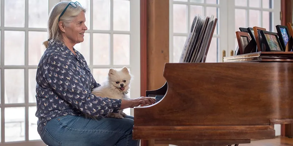 Pomerania oyendo música relajante para perros, en el regazo de su tutora que toca un piano.